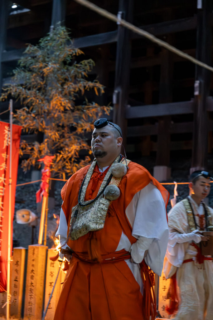 Senior priest in orange robes standing before the ritual grounds at Tanukidani Fudoin's fire walking festival