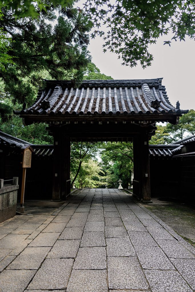 The wooden main gate of Horinji Temple in Arashiyama, Kyoto, framed by maple leave