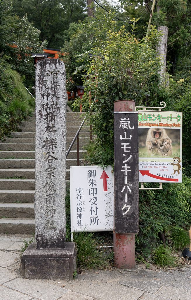 Stone marker for Ichitani-Munakata Shrine at the foot of the stairs in Arashiyama, beside an Arashiyama Monkey Park sign
