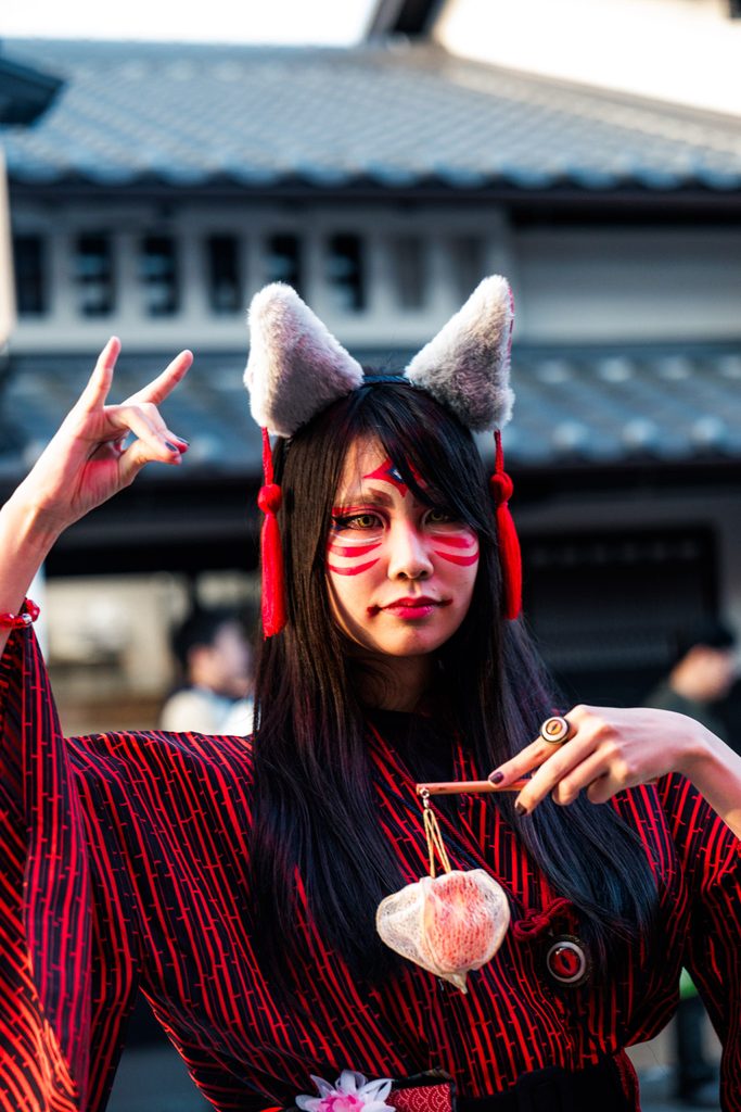 Performer in fox yokai makeup and ears on an Edo-style street