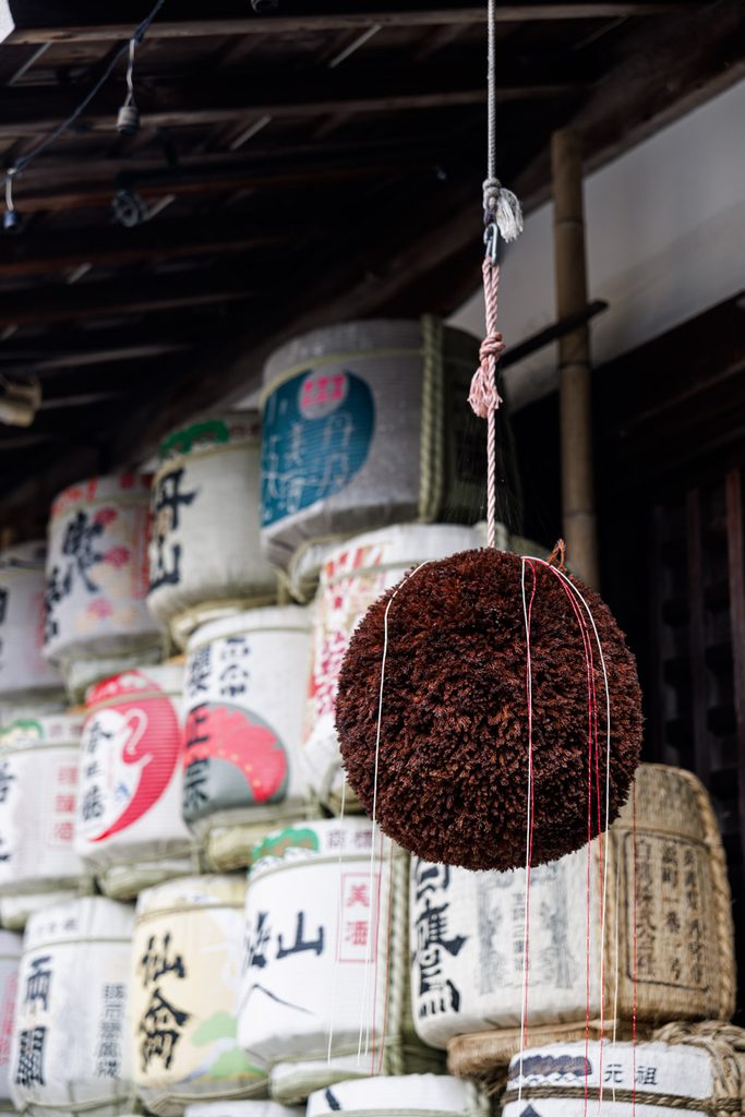 A sugidama cedar ball hanging in front of donated sake barrels at Matsuo Taisha, Kyoto's sake shrine