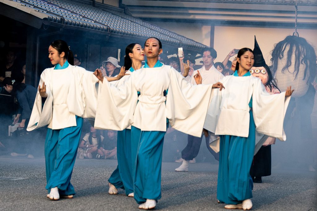 Dancers in white robes and blue hakama performing through stage smoke