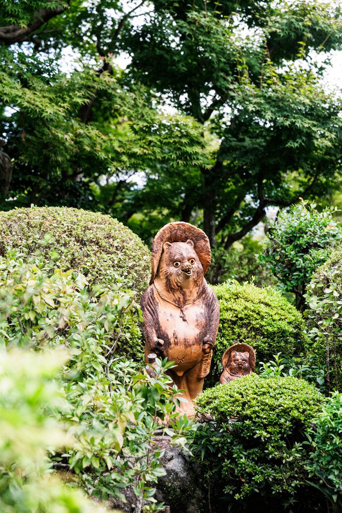 Ceramic tanuki statues among clipped shrubs in the garden at Suzumushi-dera Temple, Kyoto
