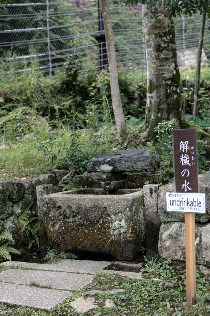 The Kaiwai no Mizu spring at Tsukiyomi Shrine in Kyoto, a mossy stone trough beside a sign reading undrinkable