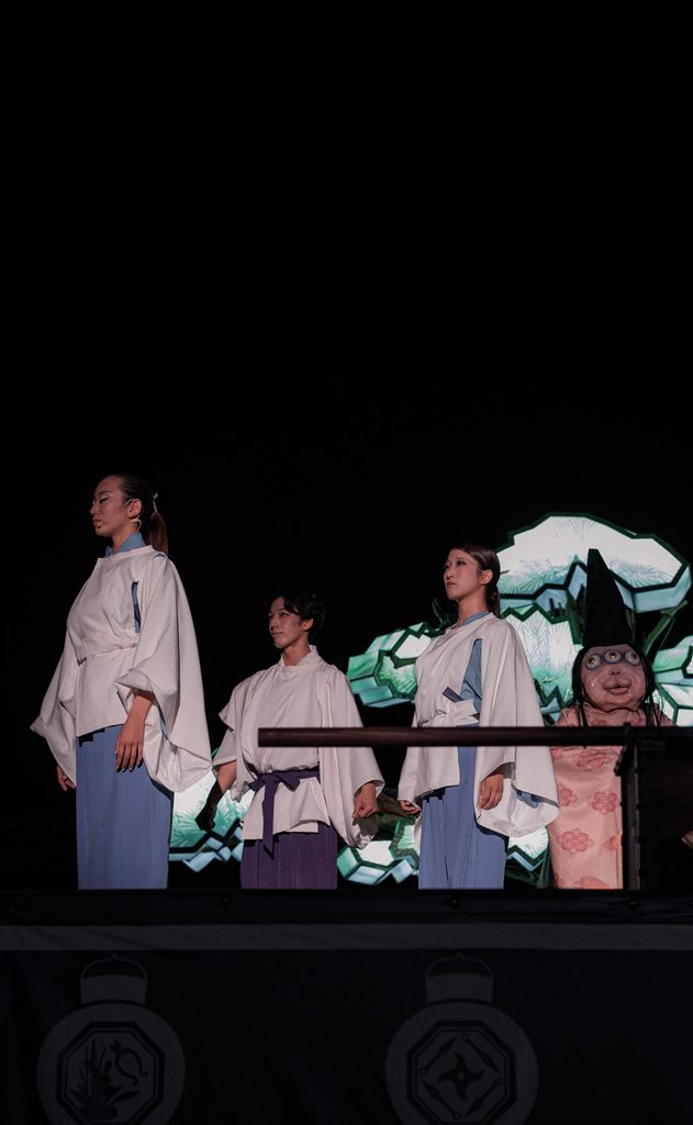 Dancers in white robes and a yokai lined up on the night stage